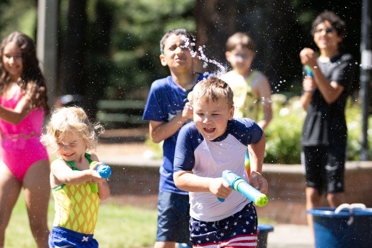 Children playing with water guns outdoors on a sunny day at summer camp, laughing and getting soaked.