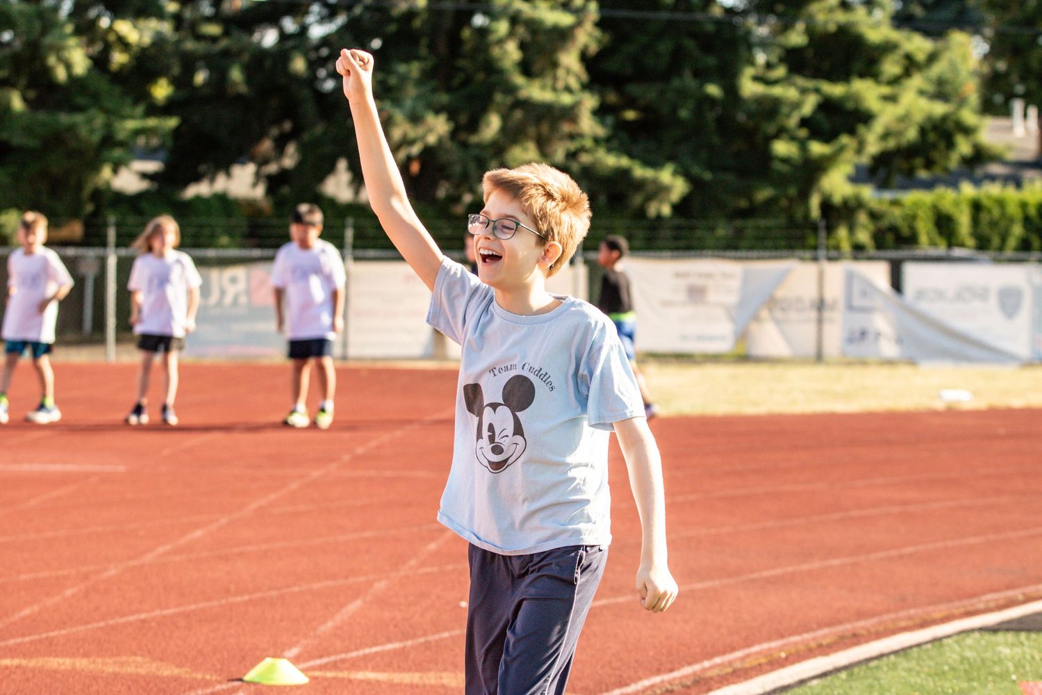 A young boy in a Mickey Mouse shirt celebrates with raised fist on a track and field during a sports event.