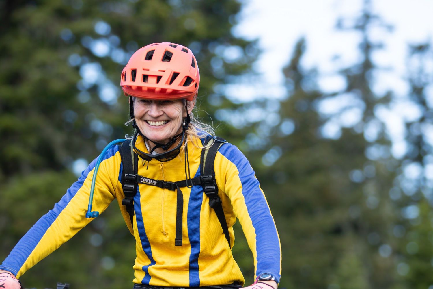 Smiling woman wearing red helmet and yellow jacket riding mountain bike outdoors.