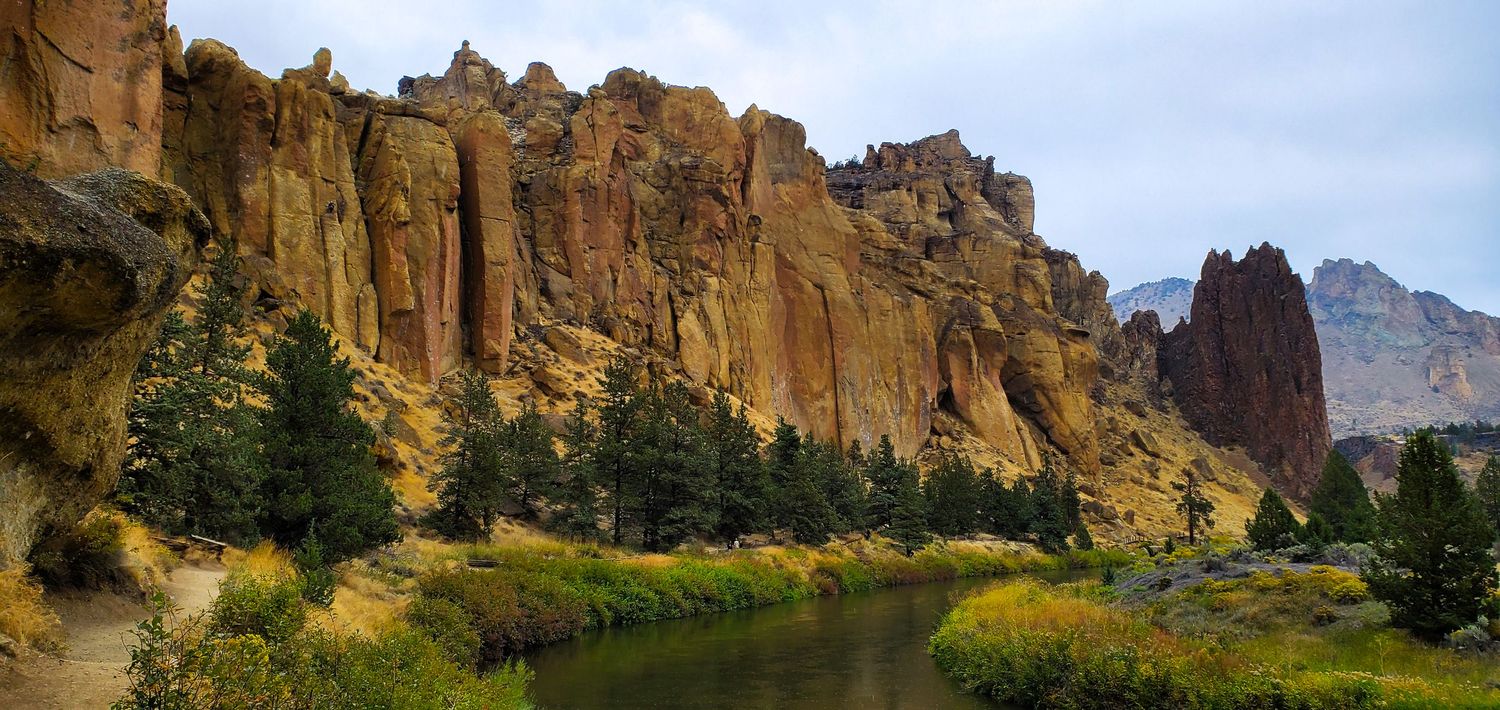 Towering golden rock formations reflect in a calm river at Smith Rock State Park, Oregon.