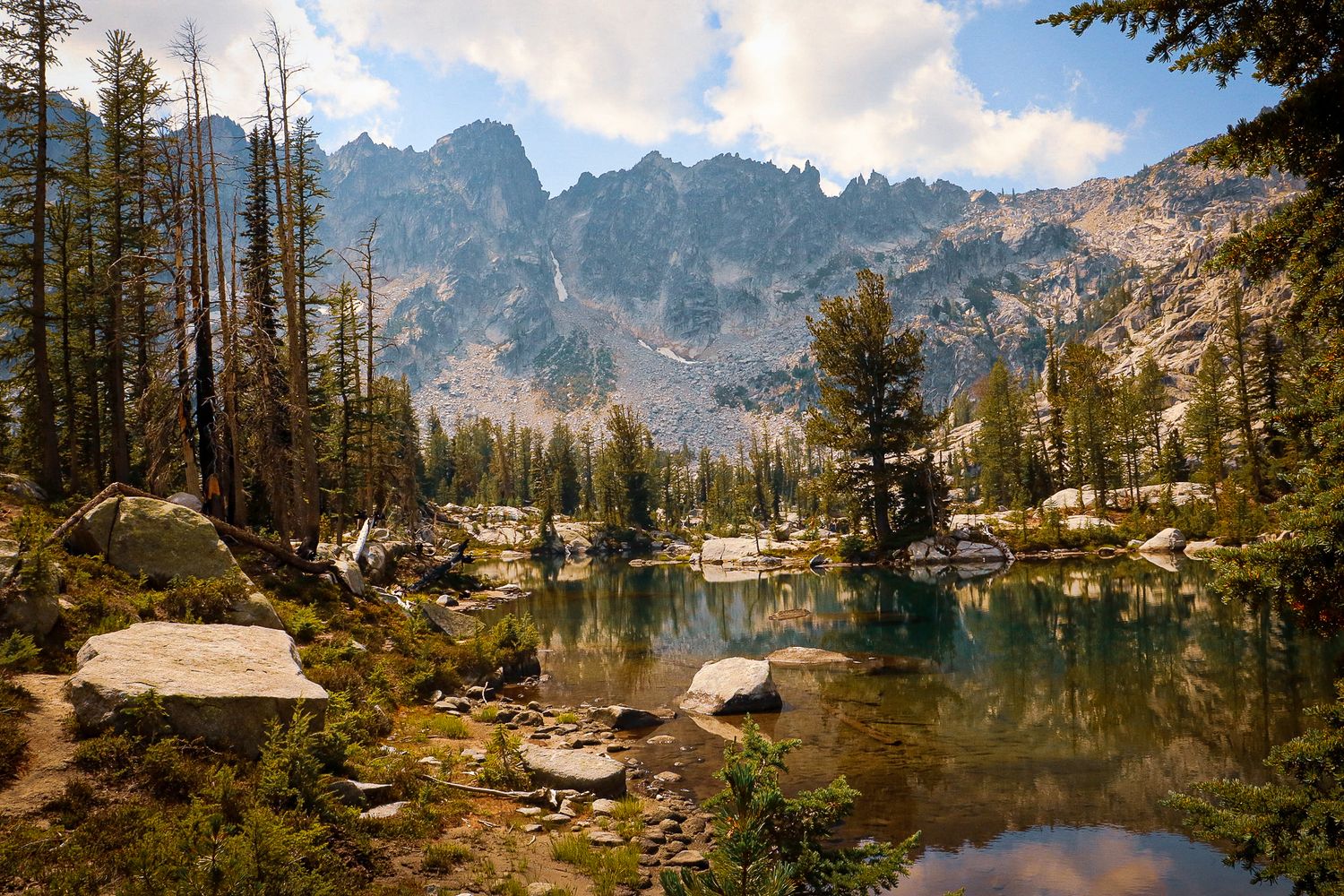 Serene alpine lake reflecting pine trees and rocky mountain peaks in a sunny wilderness landscape.
