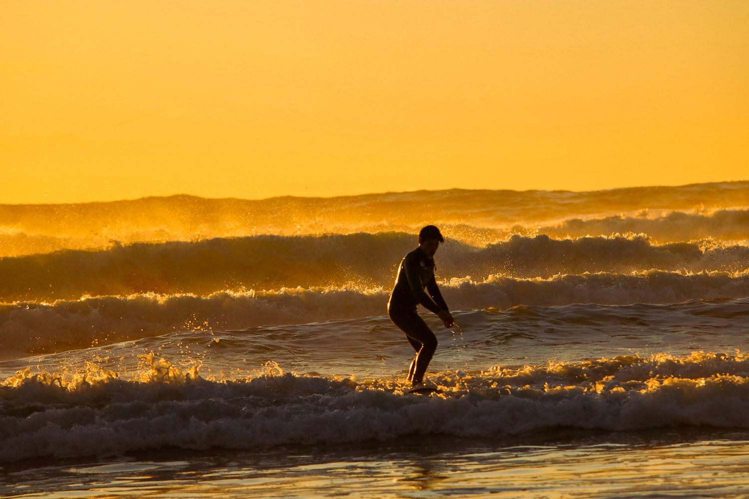 Silhouette of a surfer riding a wave during a vibrant golden ocean sunset.