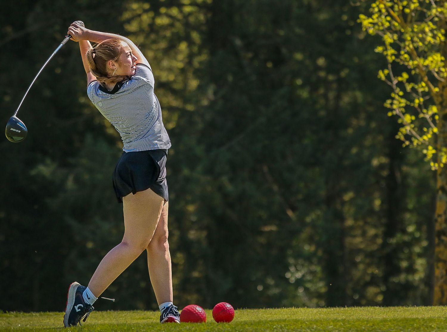 A young woman follows through on a powerful golf swing on a sunlit fairway.