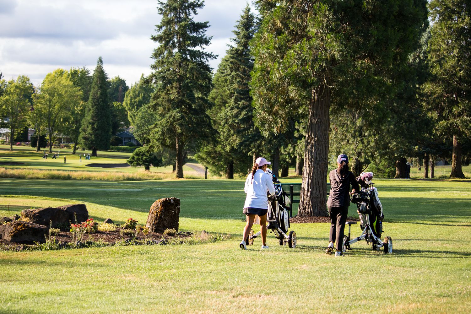 Three female golfers walk the fairway pulling golf carts on an overcast day.