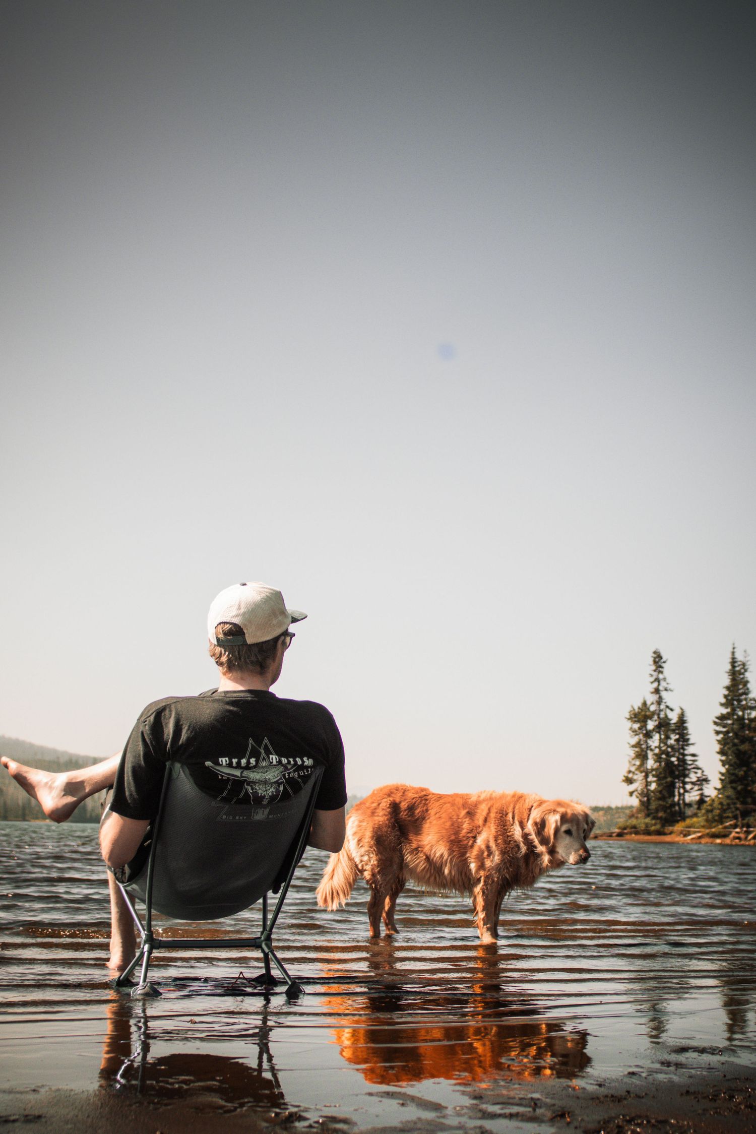 Man standing in a mountain lake beside a golden retriever during an outdoor dog photography session in Oregon.