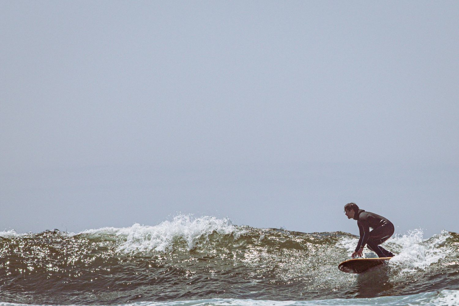 A lone surfer in a wetsuit balances on a board while riding a breaking ocean wave.