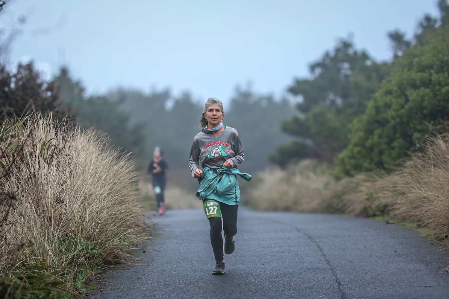 Female runner with race bib jogging on a foggy tree-lined path during a race.