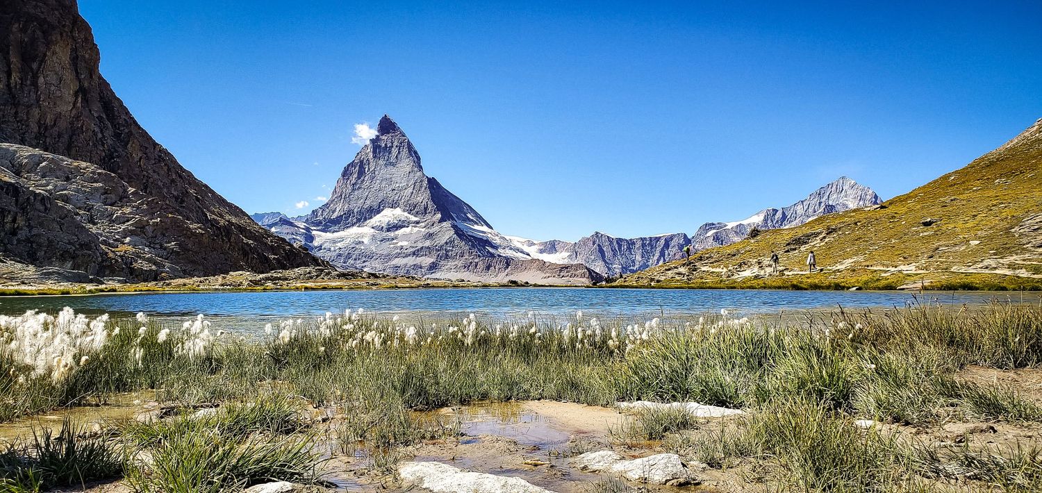 Iconic Matterhorn peak reflected in a crystal clear alpine lake under a vivid blue sky.