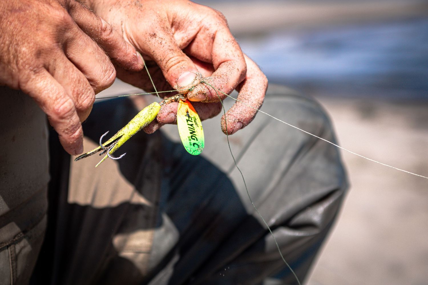 Fisherman holding a bright yellow and green fishing lure with hooks attached to a fishing line outdoors.