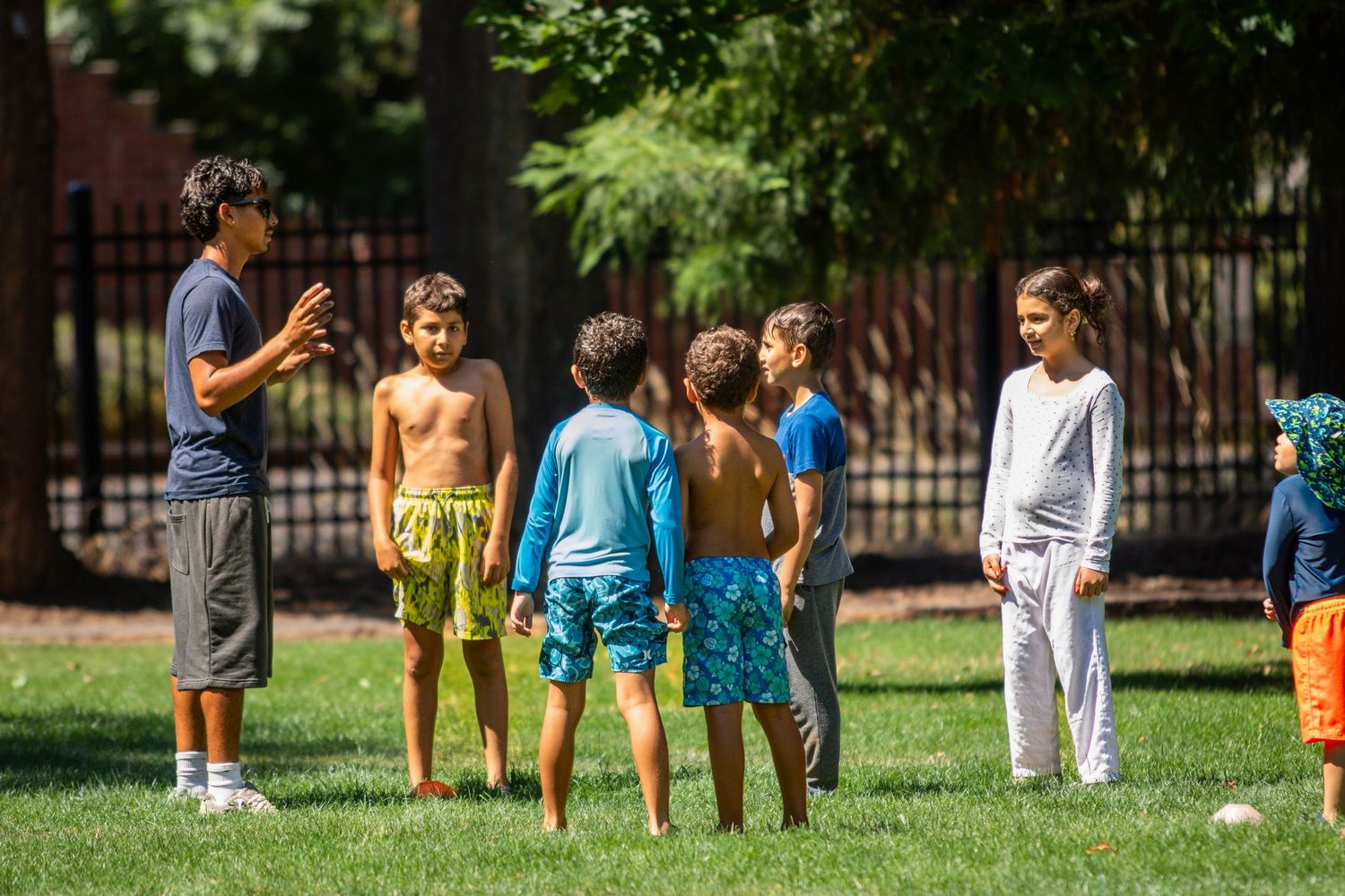 Youth sports coach instructing group of children on green grass field in summer.