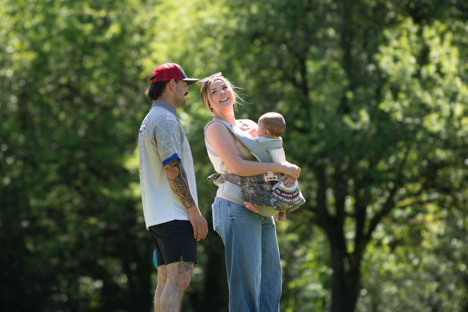 Young family with a baby enjoying a sunny day outdoors surrounded by green trees.