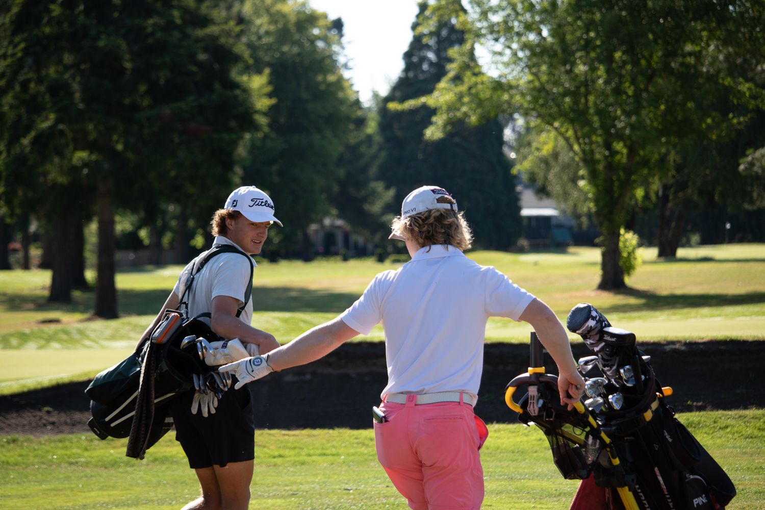 Two golfers in matching caps review club selections from their bags on a sunny fairway.