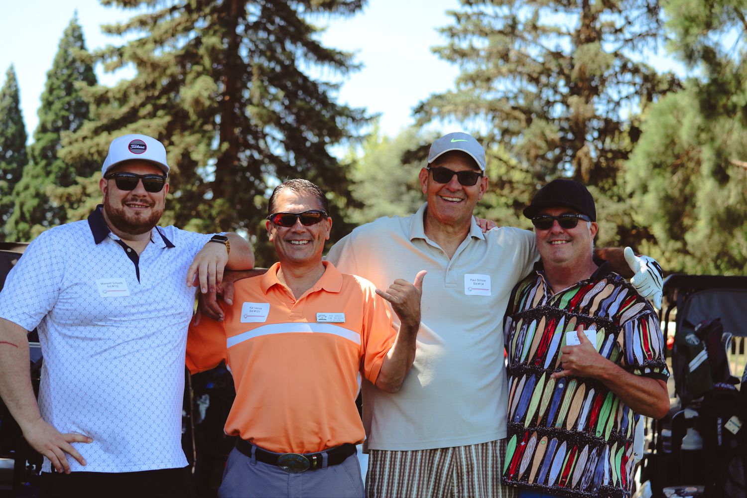 Four men smiling and posing together outdoors at a golf course on a sunny day.