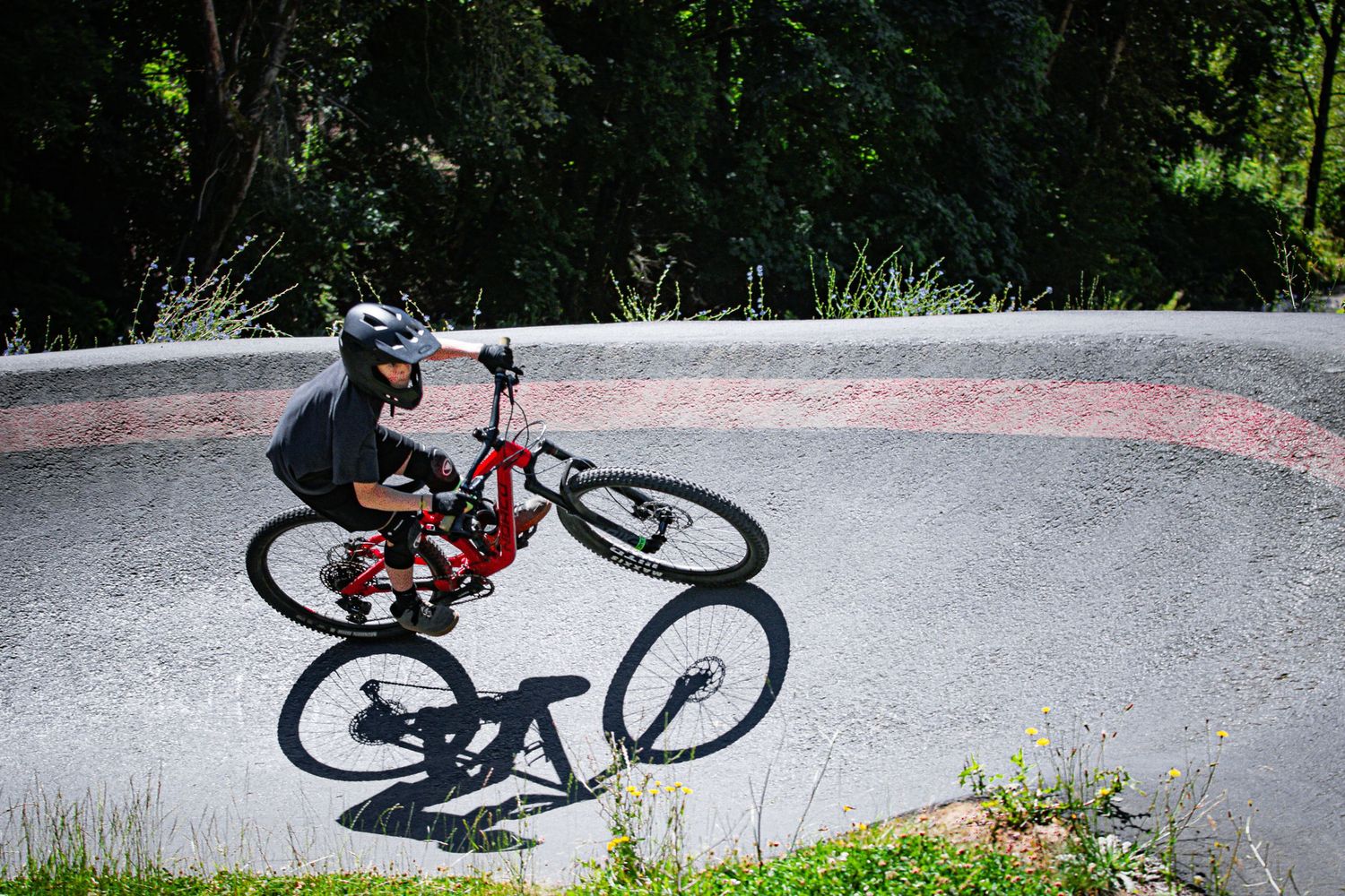 Cyclist performing wheelie on red mountain bike at a concrete pump track park.