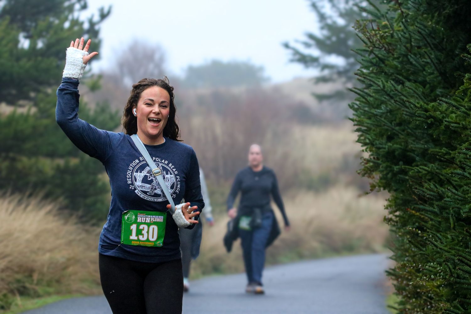 Happy female runner wearing bib 130 waving on a misty outdoor race course.