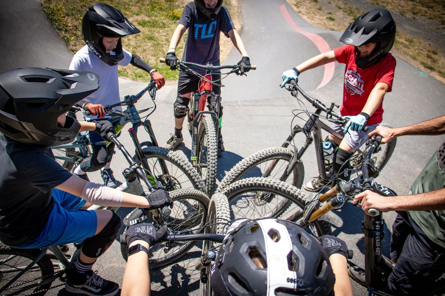 A group of young mountain bikers huddle together touching their bike wheels in a team circle.