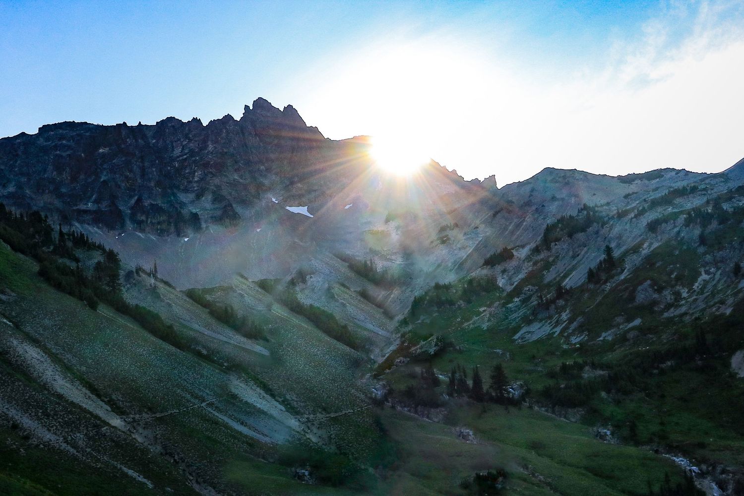 Stunning sunrise bursting over rugged green mountain peaks with misty valleys below.