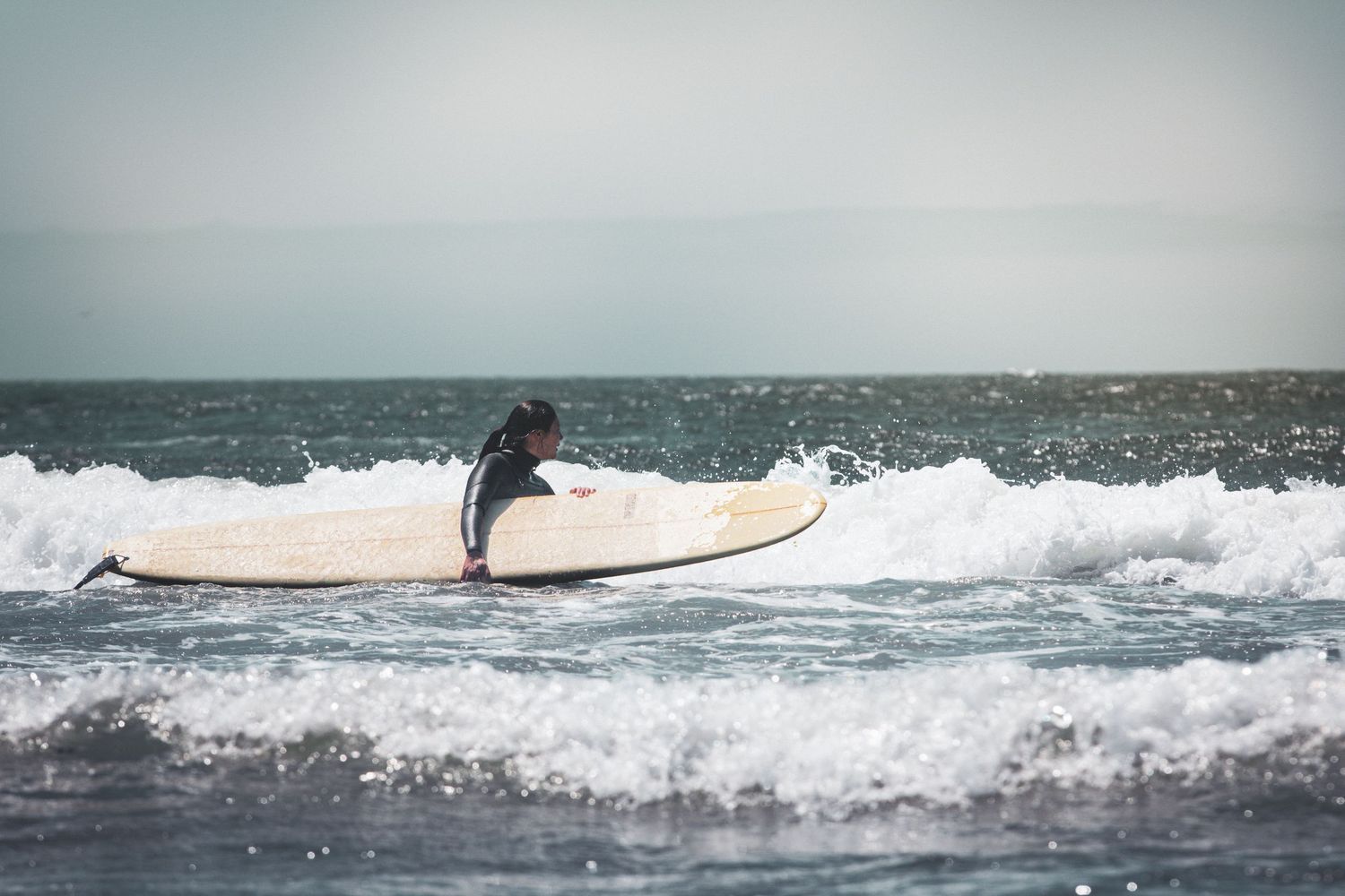 A surfer paddling through ocean waves on a white surfboard in the sea.