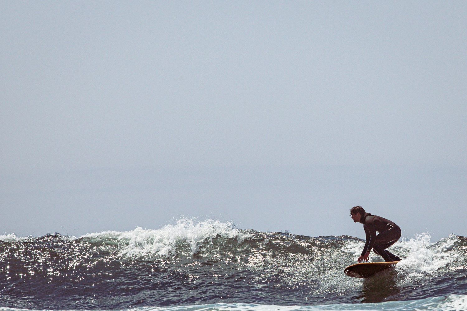 A surfer in a wetsuit riding a small wave on a calm overcast ocean day.