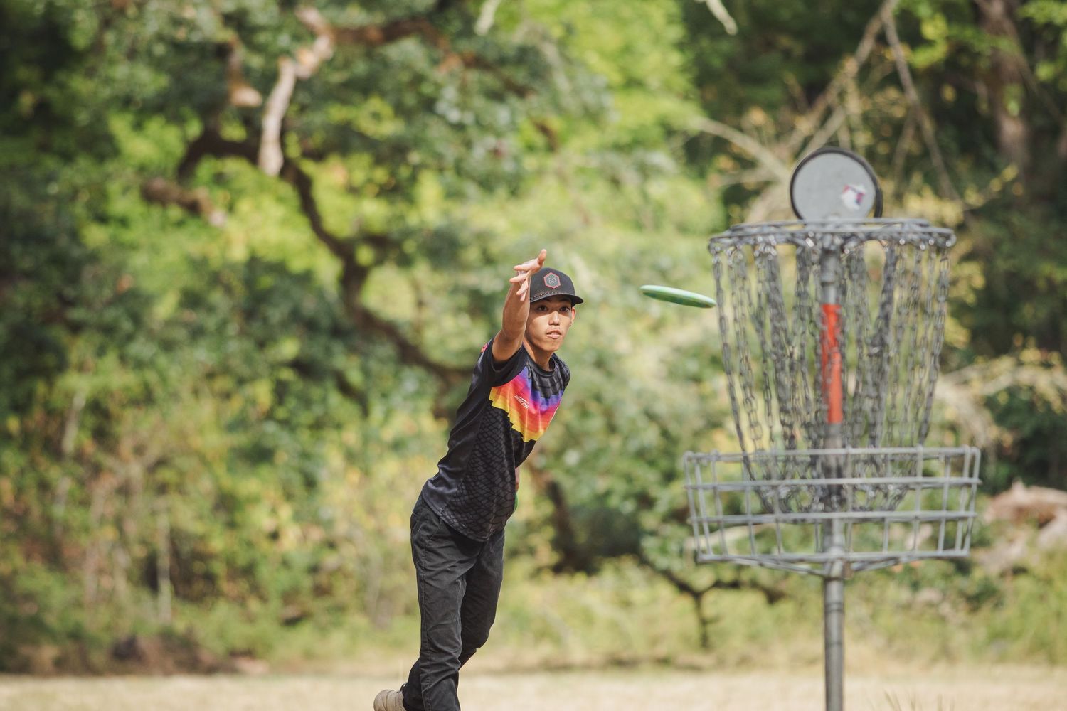 Young disc golfer throwing a frisbee toward a chain basket target outdoors.