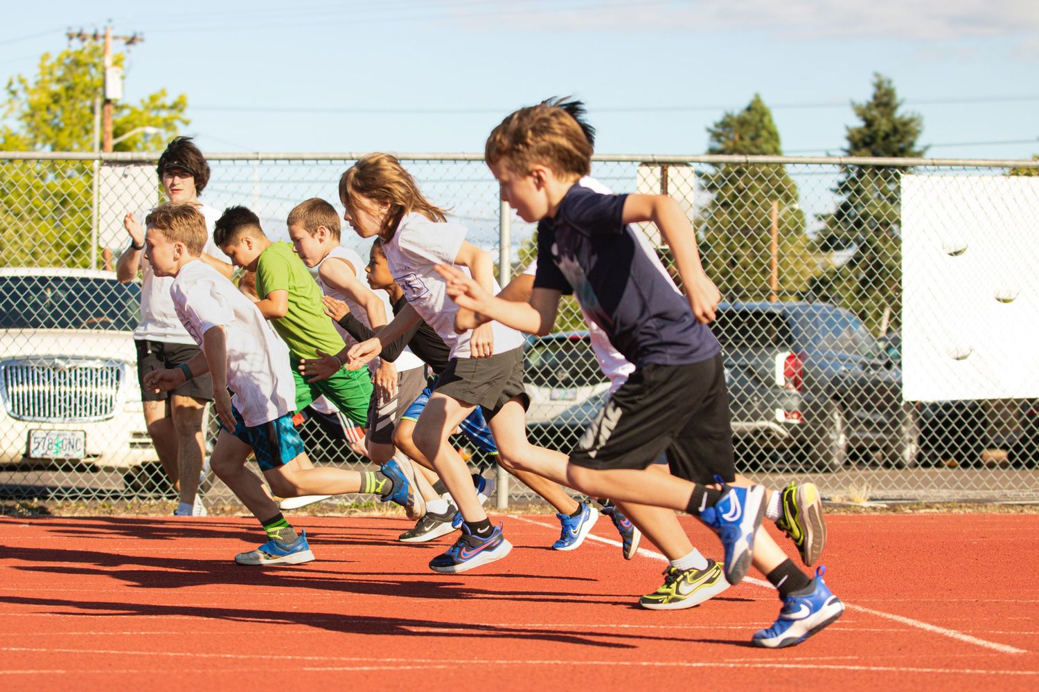 Group of children sprinting from starting line on a red outdoor running track.