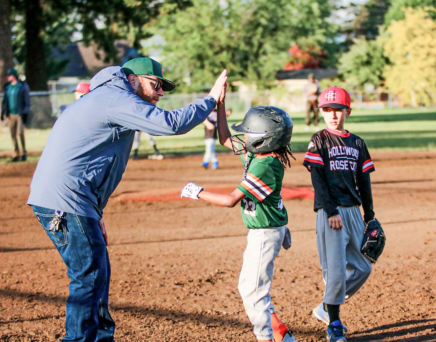 A baseball coach gives a high-five to a young player in a helmet during a youth baseball game.