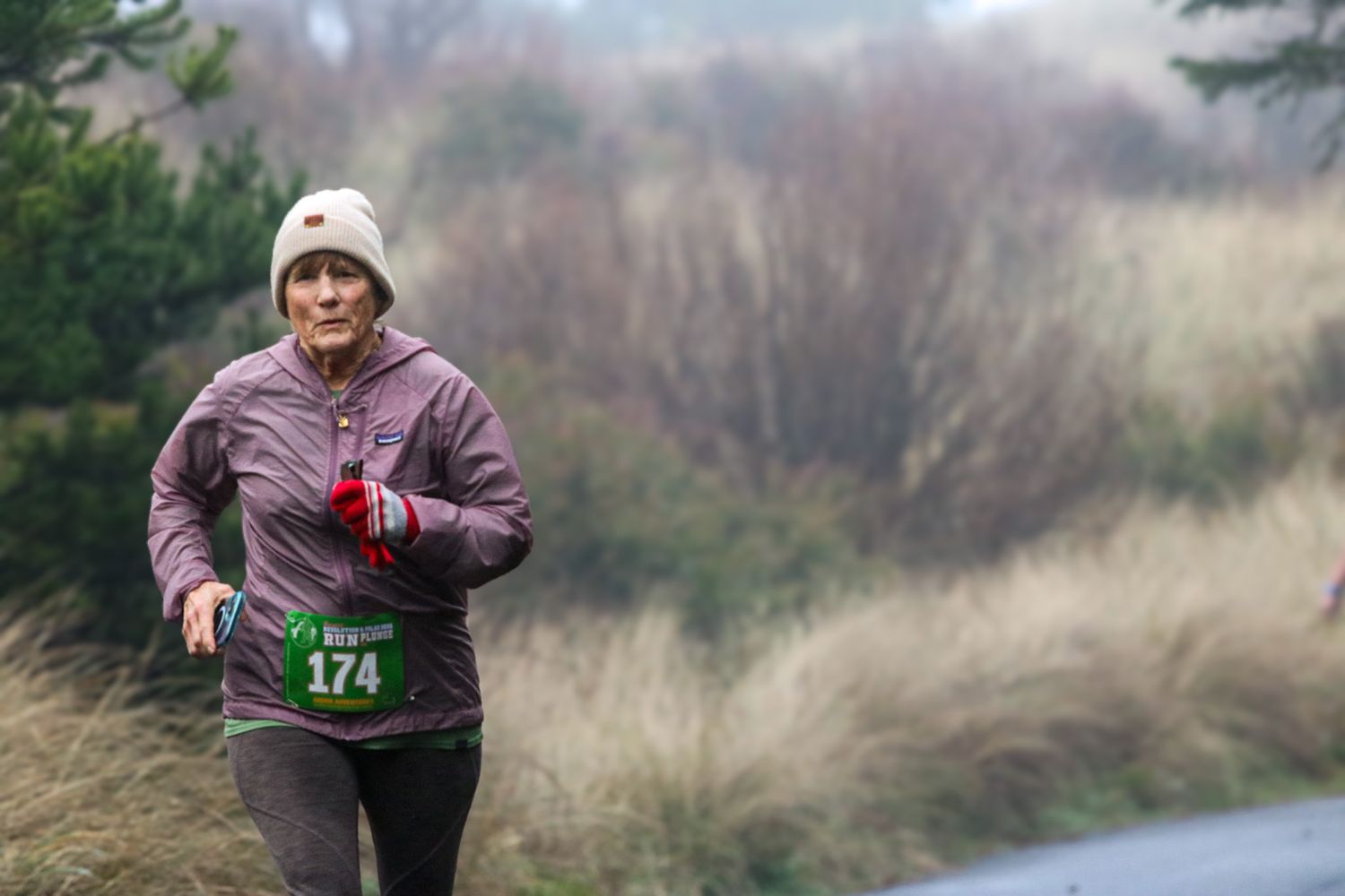 A woman wearing bib number 174 runs a road race on a foggy, overcast day.