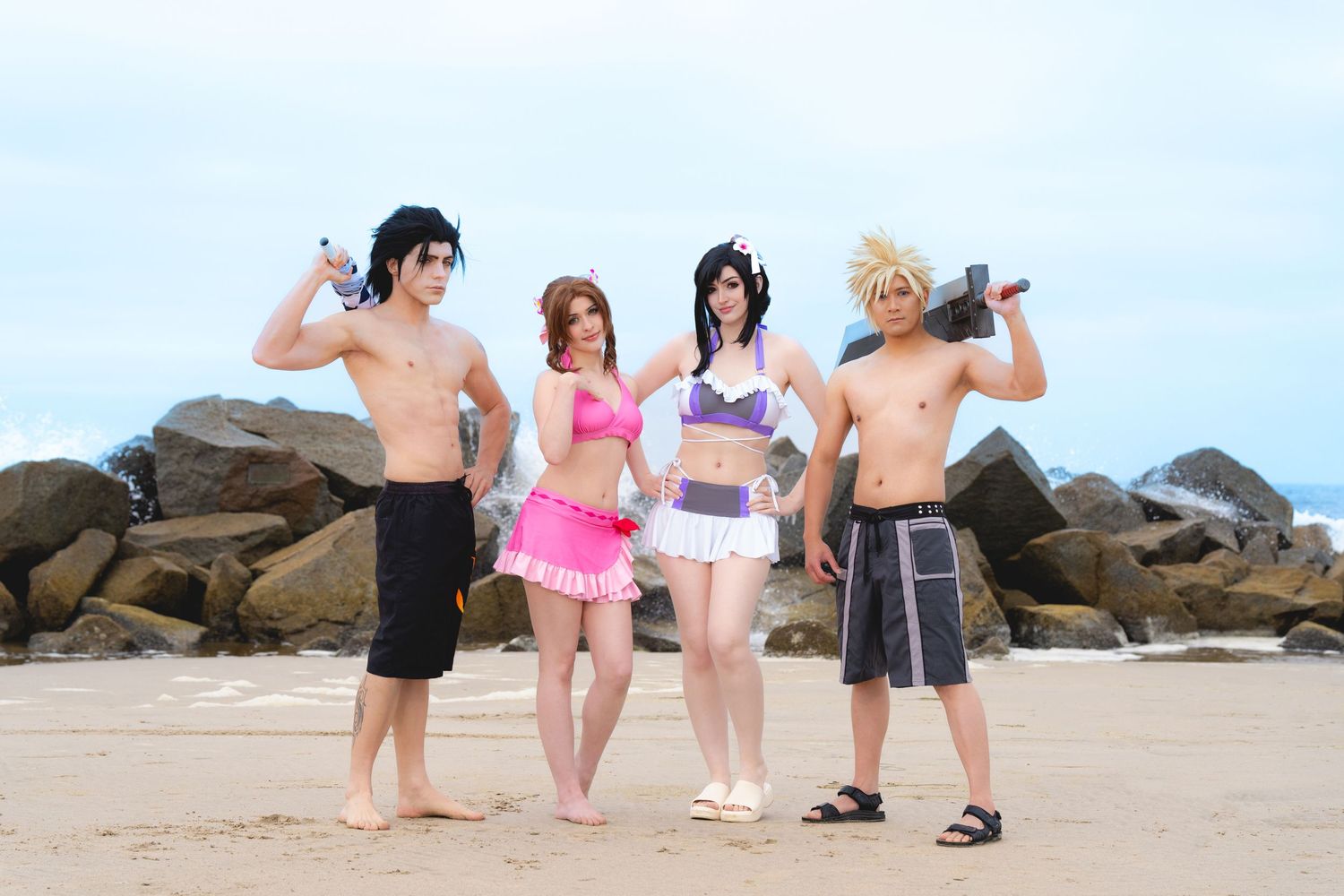 Four cosplayers in Final Fantasy beach outfits posing on rocky shoreline.