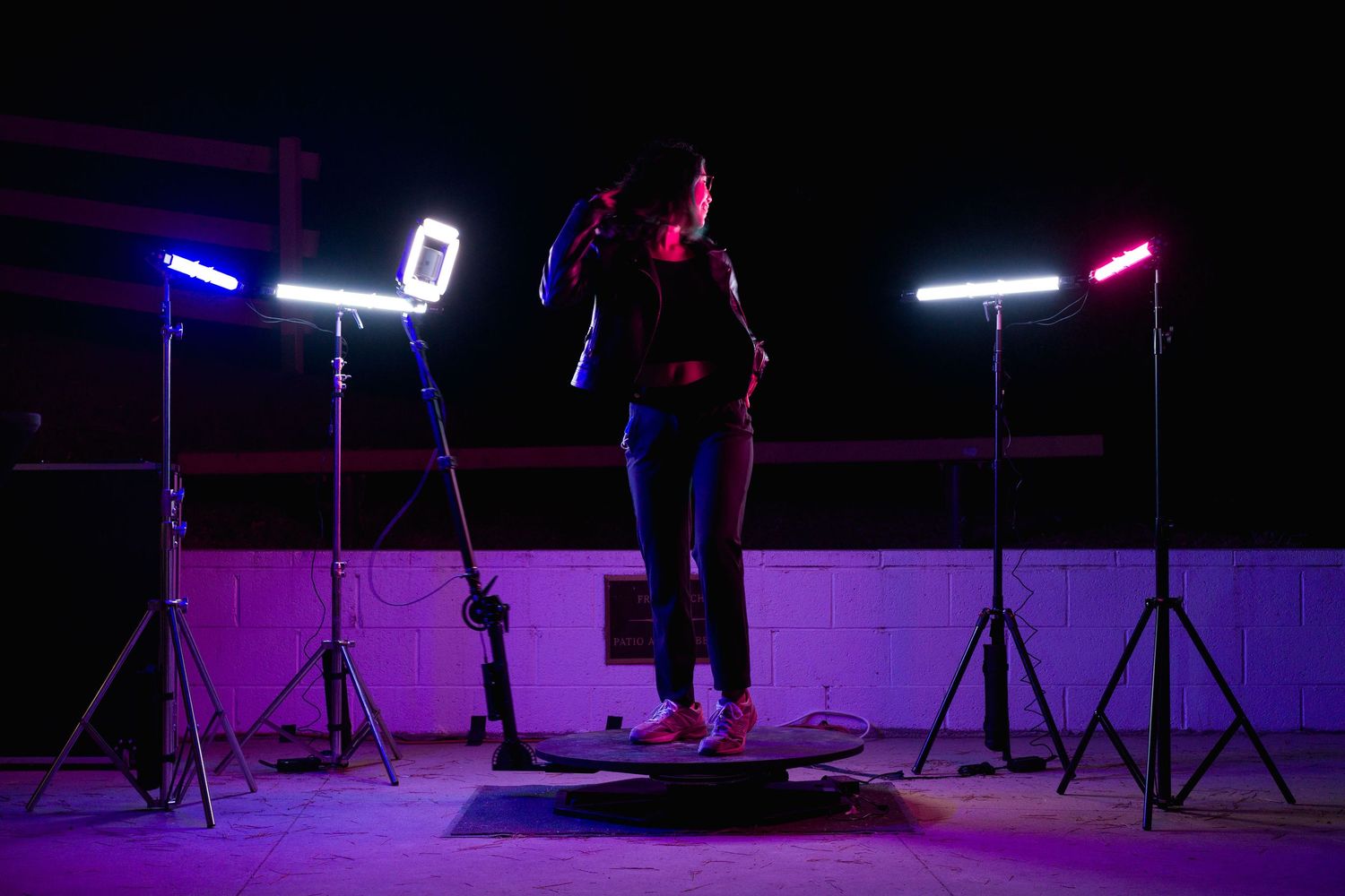 A person stands on a rotating platform surrounded by professional RGB studio lights outdoors at night.