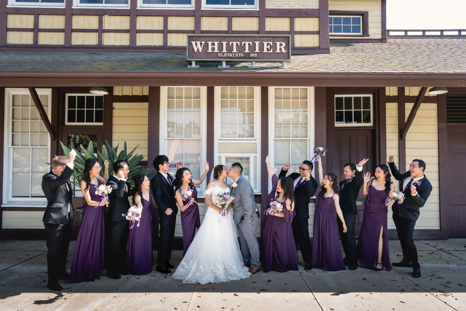 Wedding party in purple bridesmaid dresses celebrates outside Whittier train station.