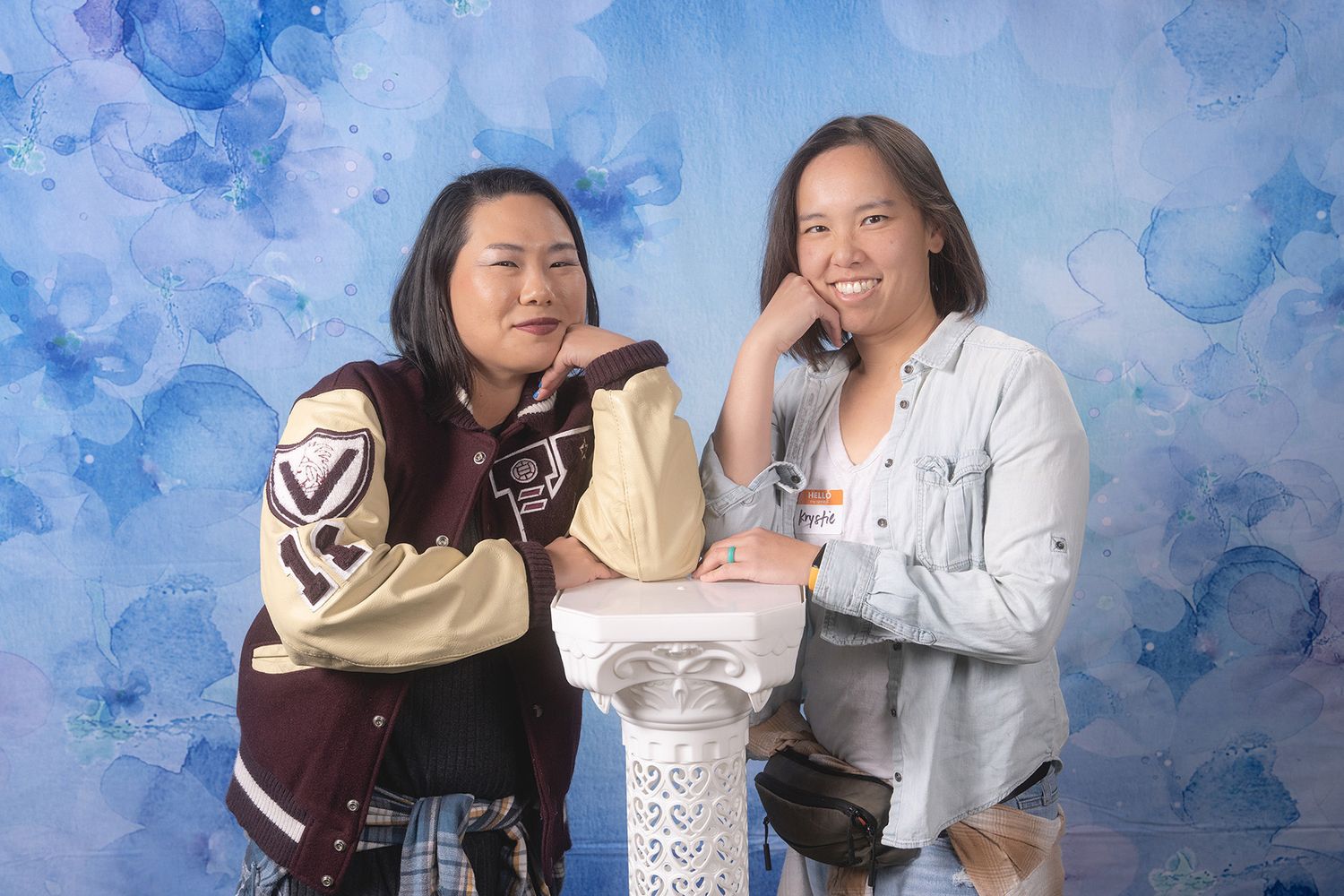Two young women pose together in front of a blue watercolor backdrop for a portrait photo.