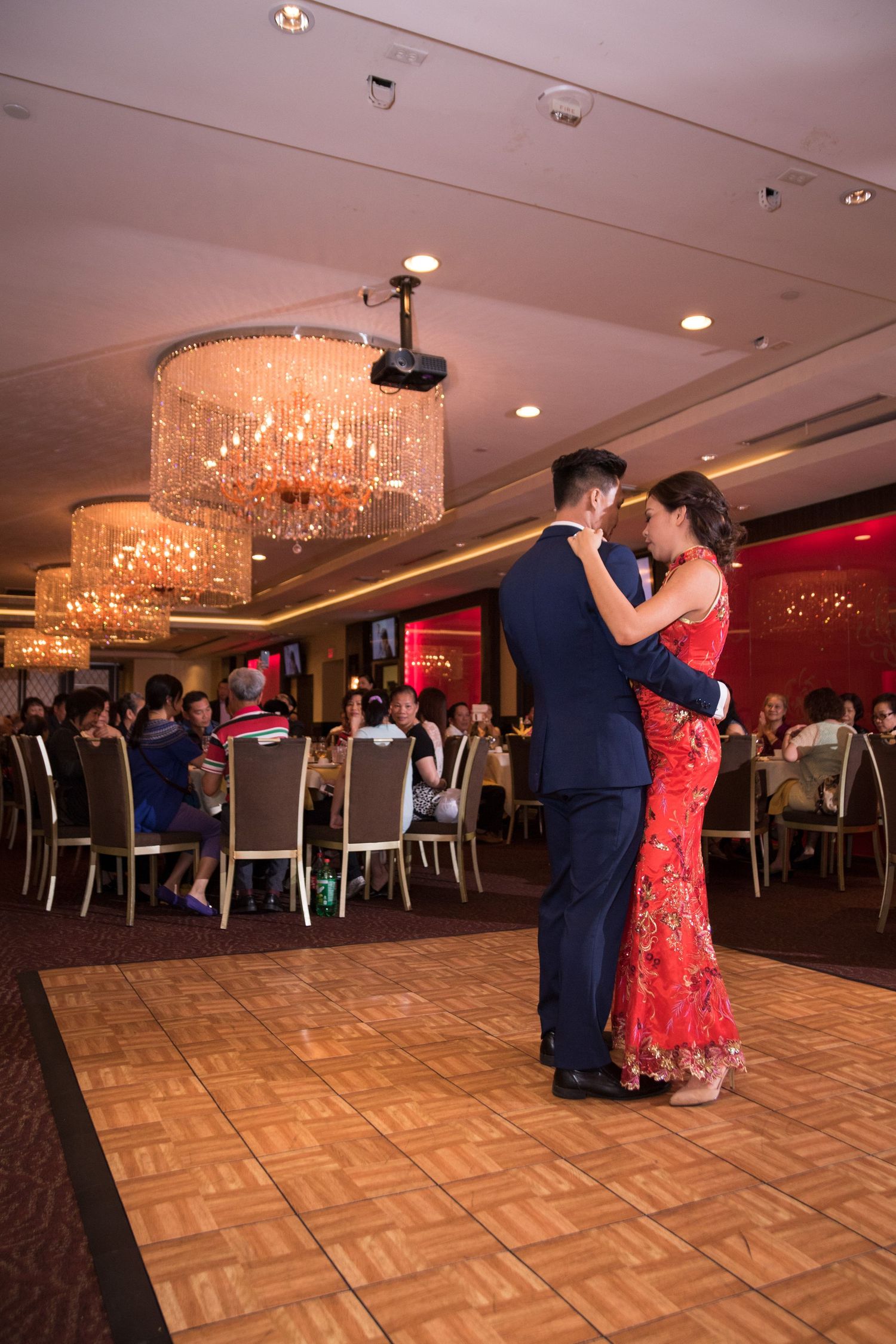 Couple shares first dance in ballroom, bride wearing red Chinese qipao dress.