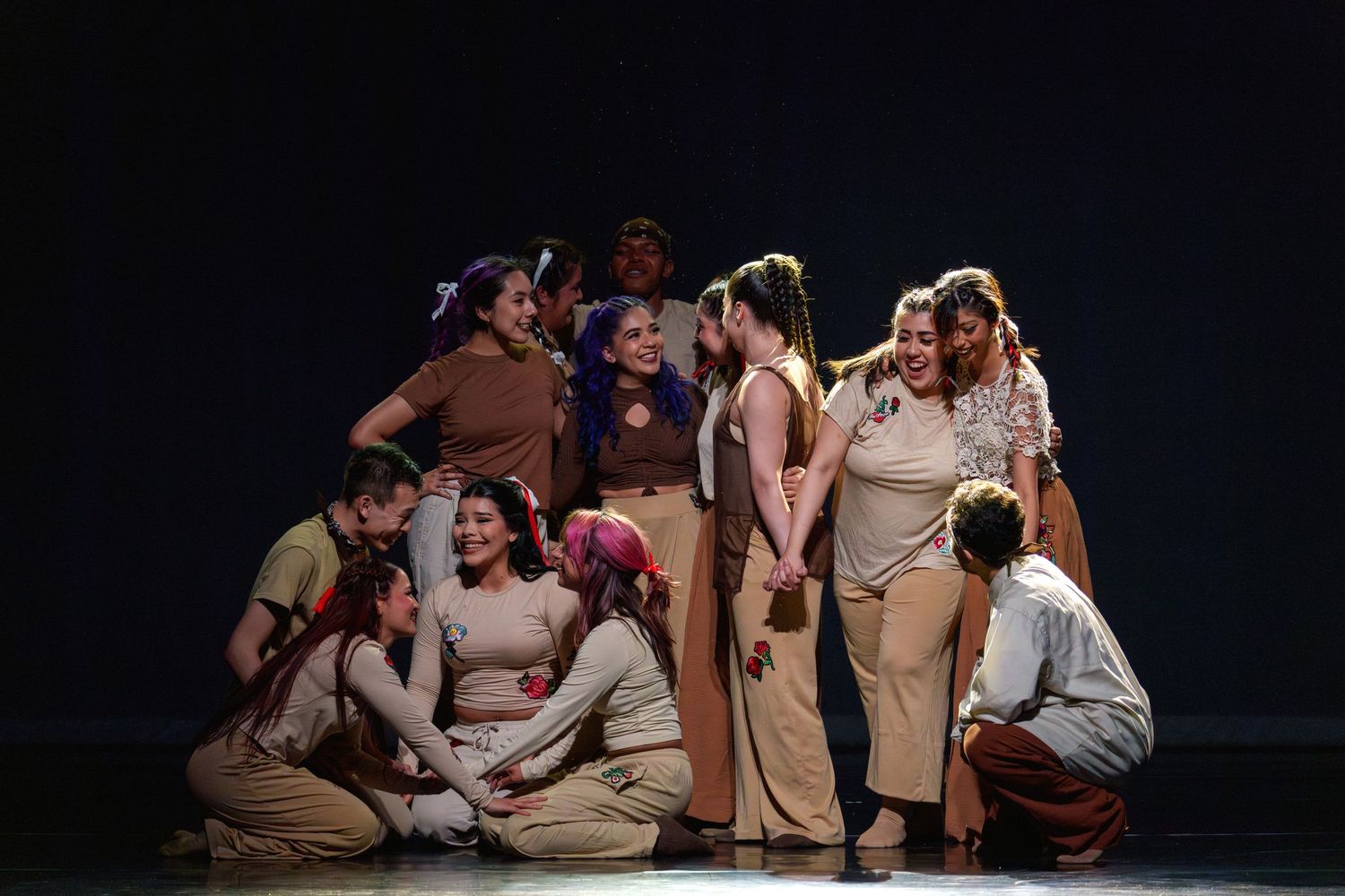 Large ensemble cast performs an emotional theatrical scene on a dimly lit stage.