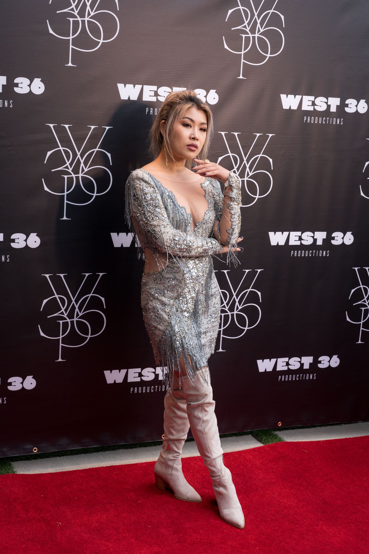 Woman in silver sequin dress and white boots poses on red carpet at West 36 Productions event.