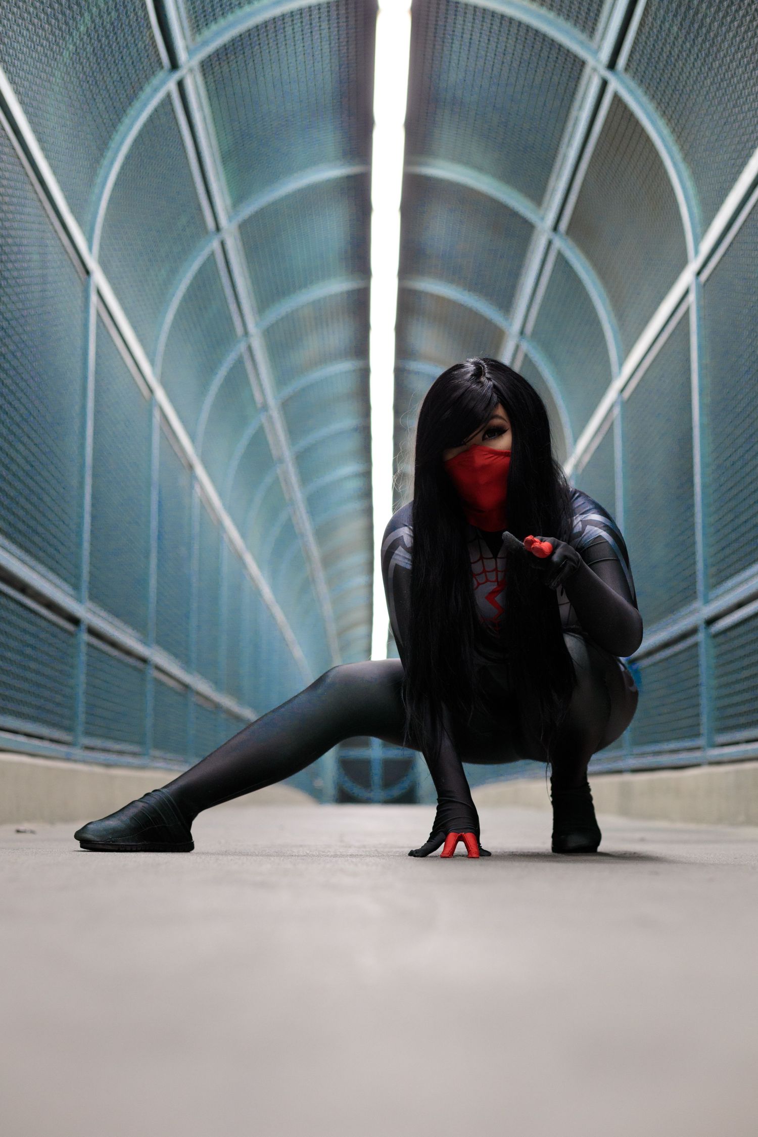 Woman in black spider-man cosplay costume crouching in a futuristic tunnel corridor.