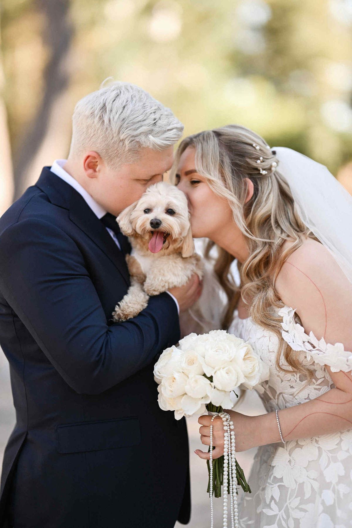 Bride and groom kissing their small pet dog outdoors at their destination wedding