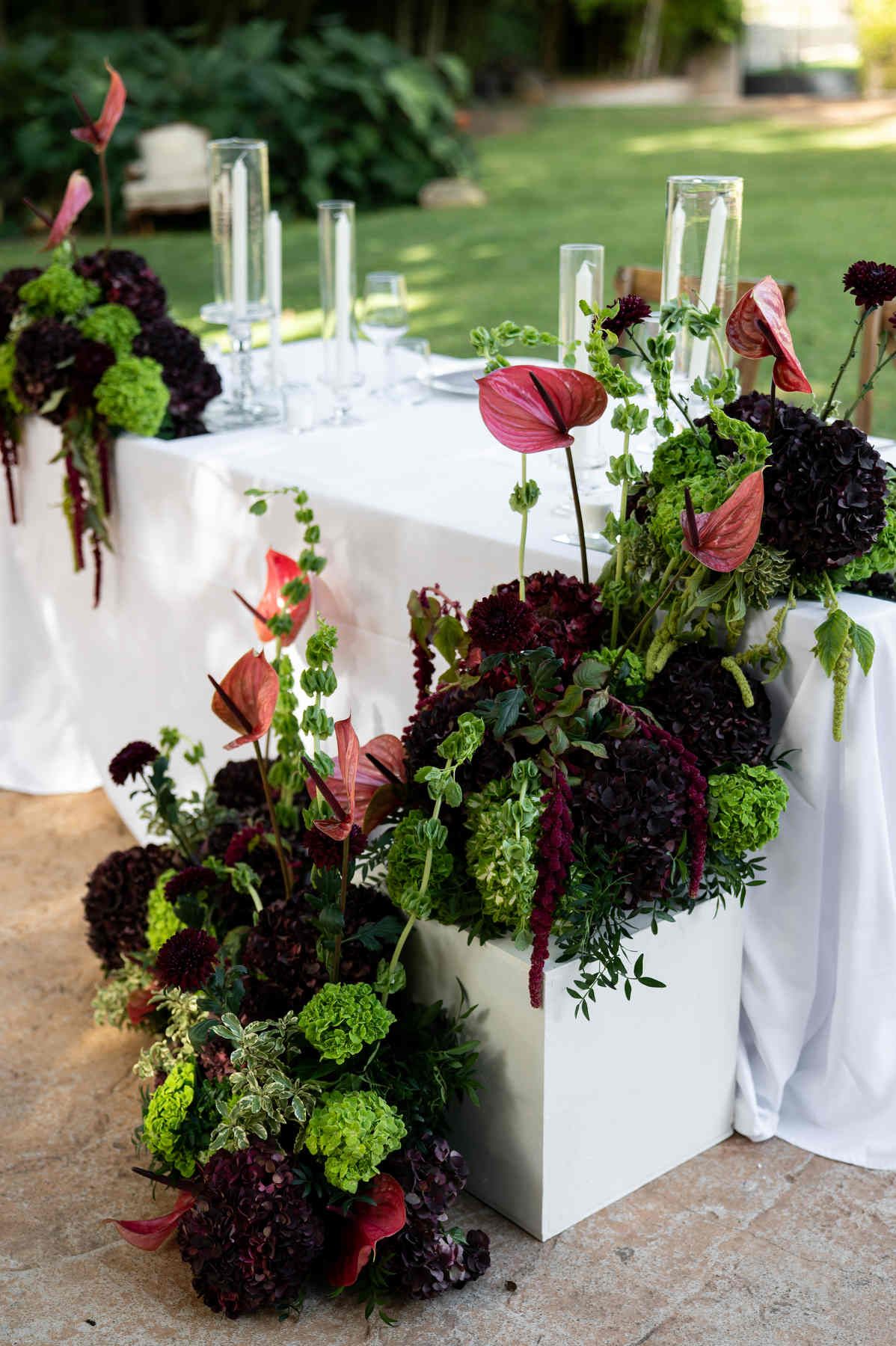 Dramatic wedding table decor with burgundy blooms and red anthuriums cascading onto the patio at Casa Santonja.