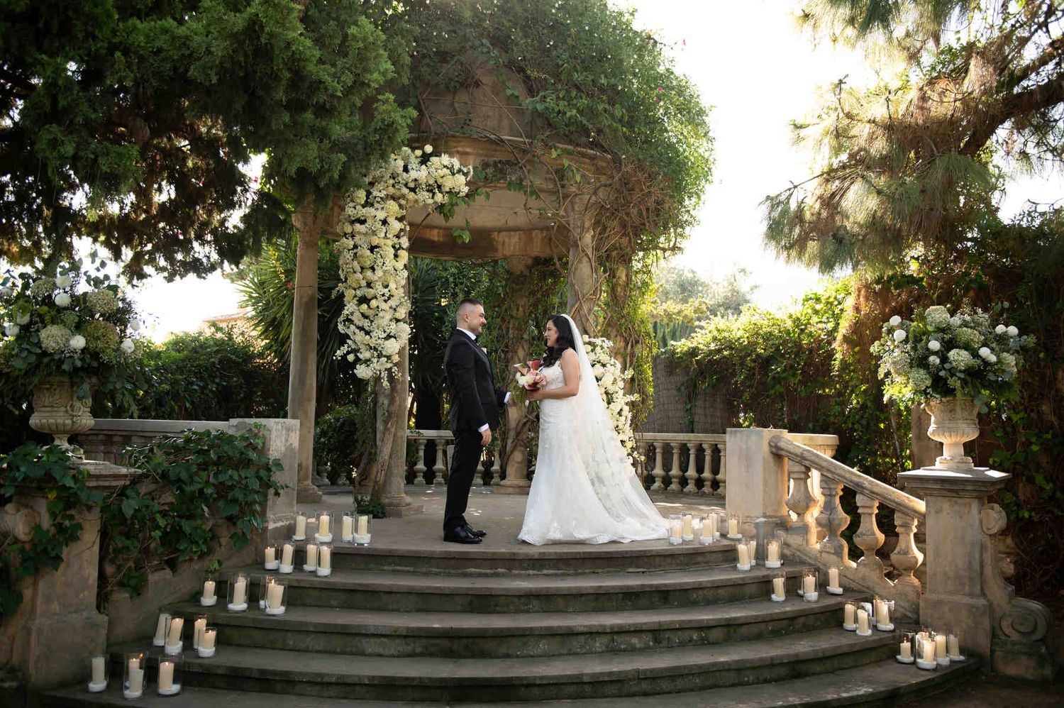 Bride and groom standing together during the wedding ceremony by a floral gazebo decorated with candles at Casa Santonja