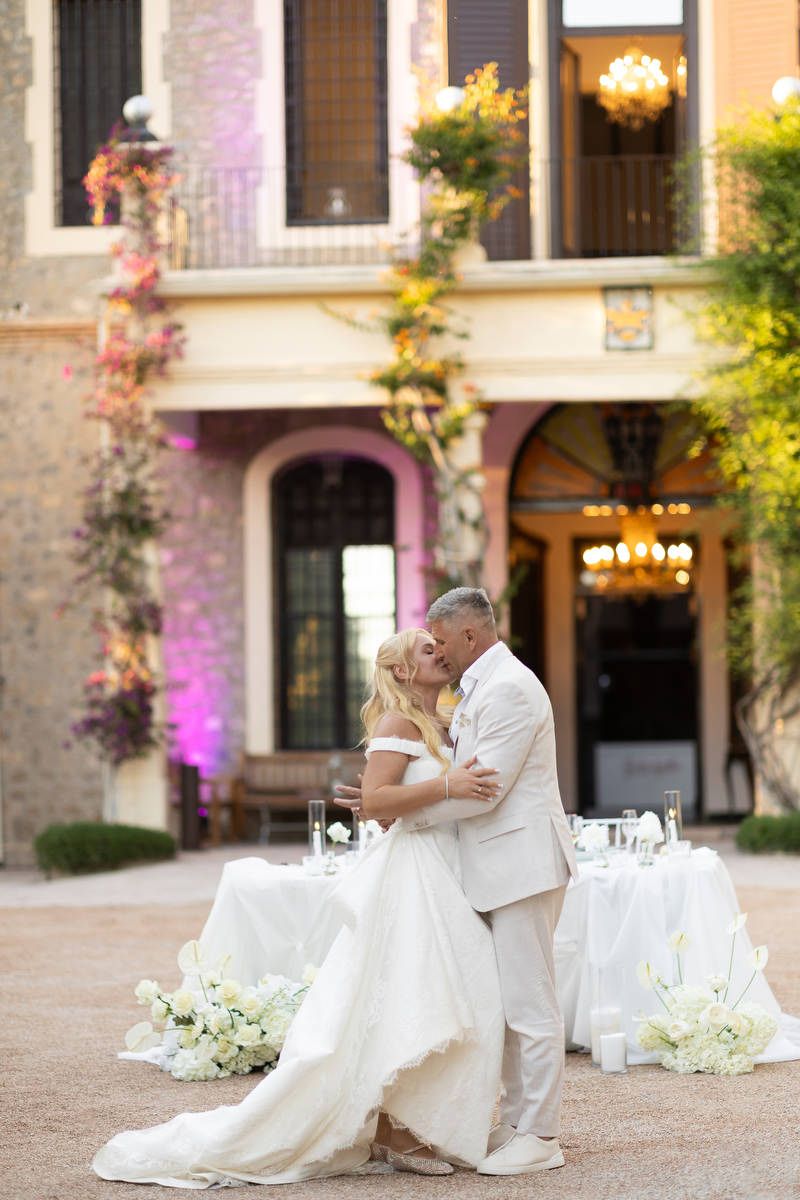 Bride and groom kissing near their dinner table outside a historic Costa Blanca building lit with pink architectural lighting.