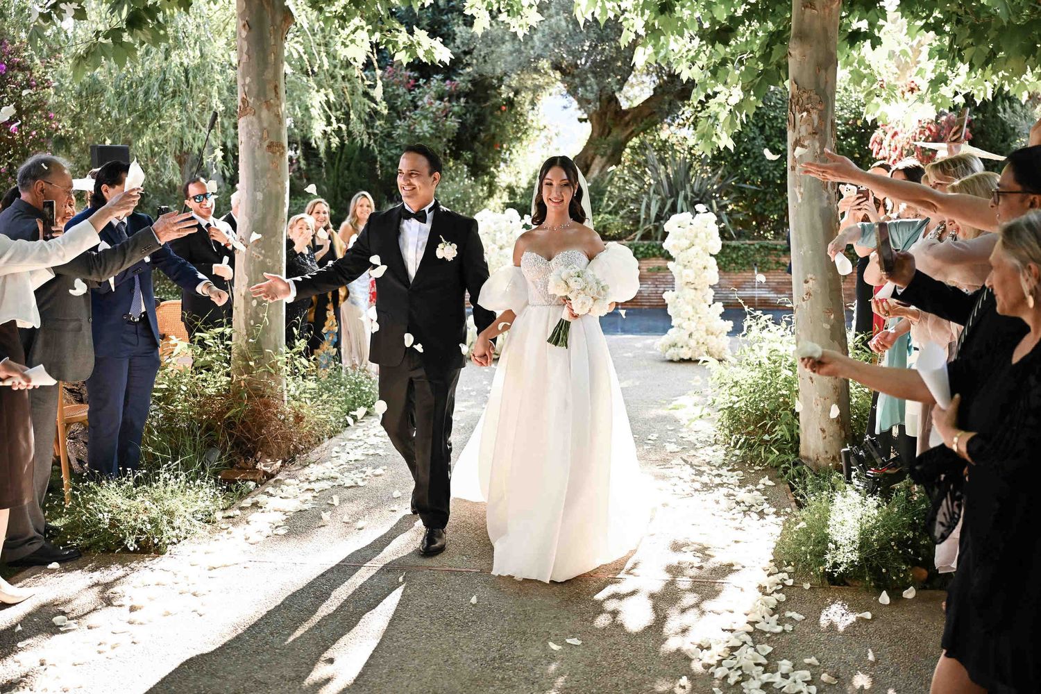 Newlyweds walking down the aisle while guests throw white petals at an outdoor garden wedding planned in Valencia.