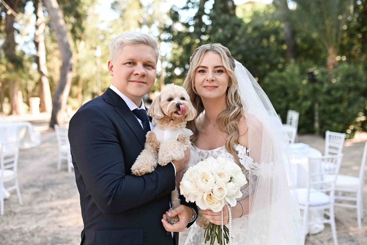 Smiling bride and groom posing with their small dog dressed for the occasion at their outdoor destination wedding in Benidorm