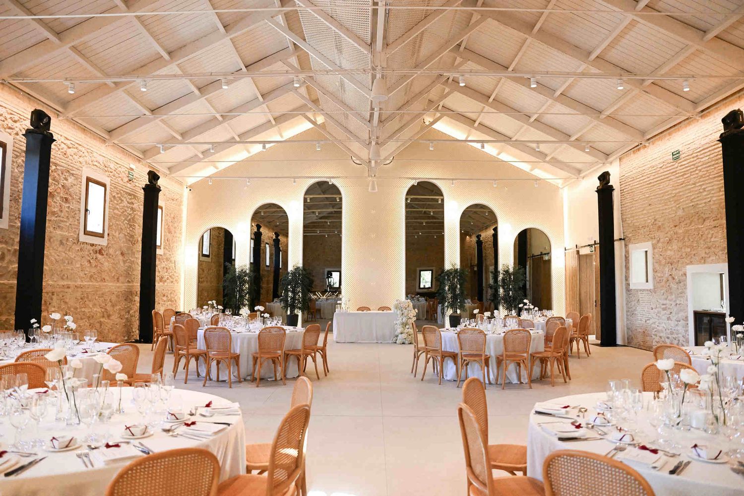 Elegant indoor wedding reception setup with round tables and arched mirrors inside the historic hall at Finca del Canónigo.
