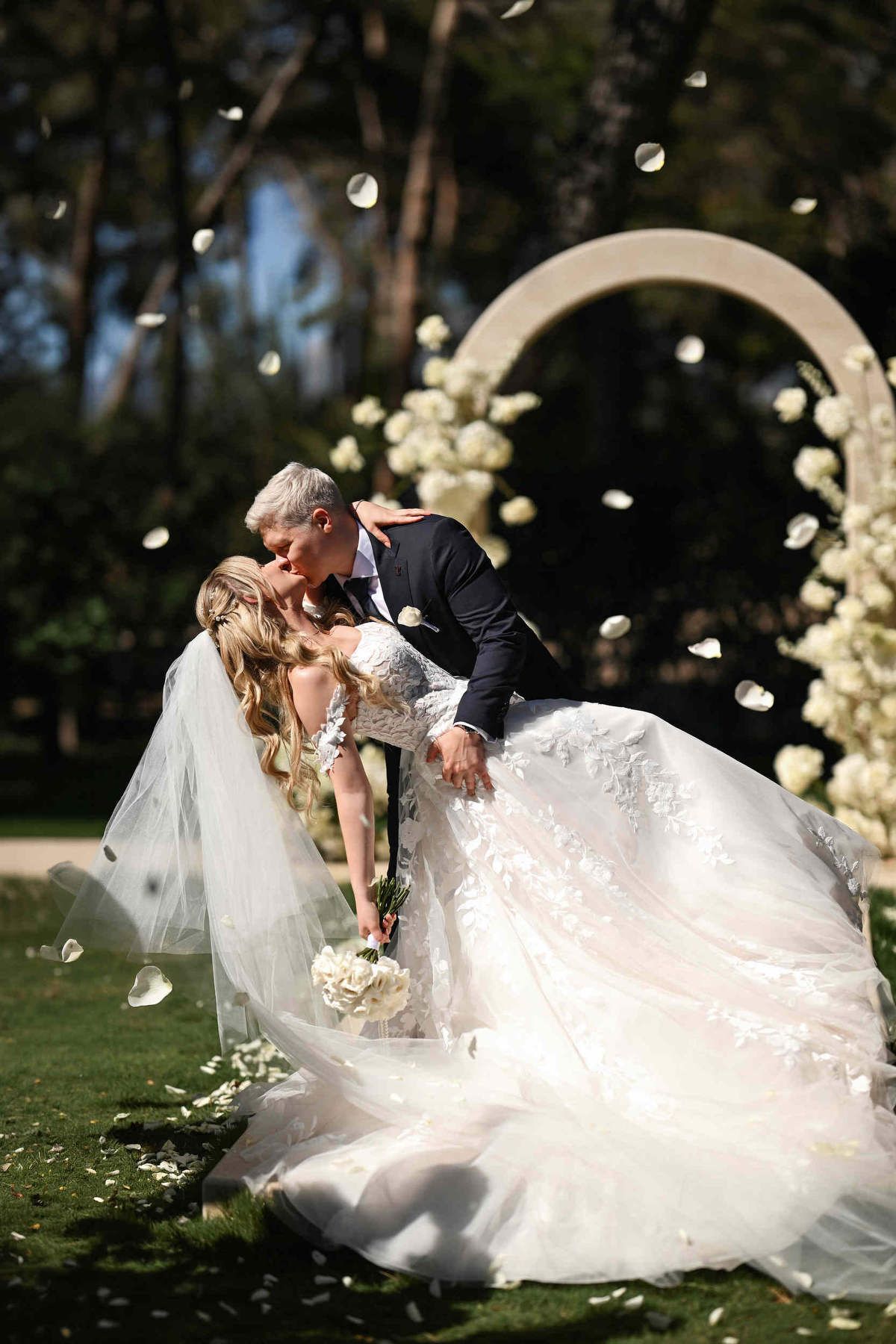 Groom dipping and kissing the bride outdoors while white rose petals fall during their Finca El Senyoret wedding ceremony.