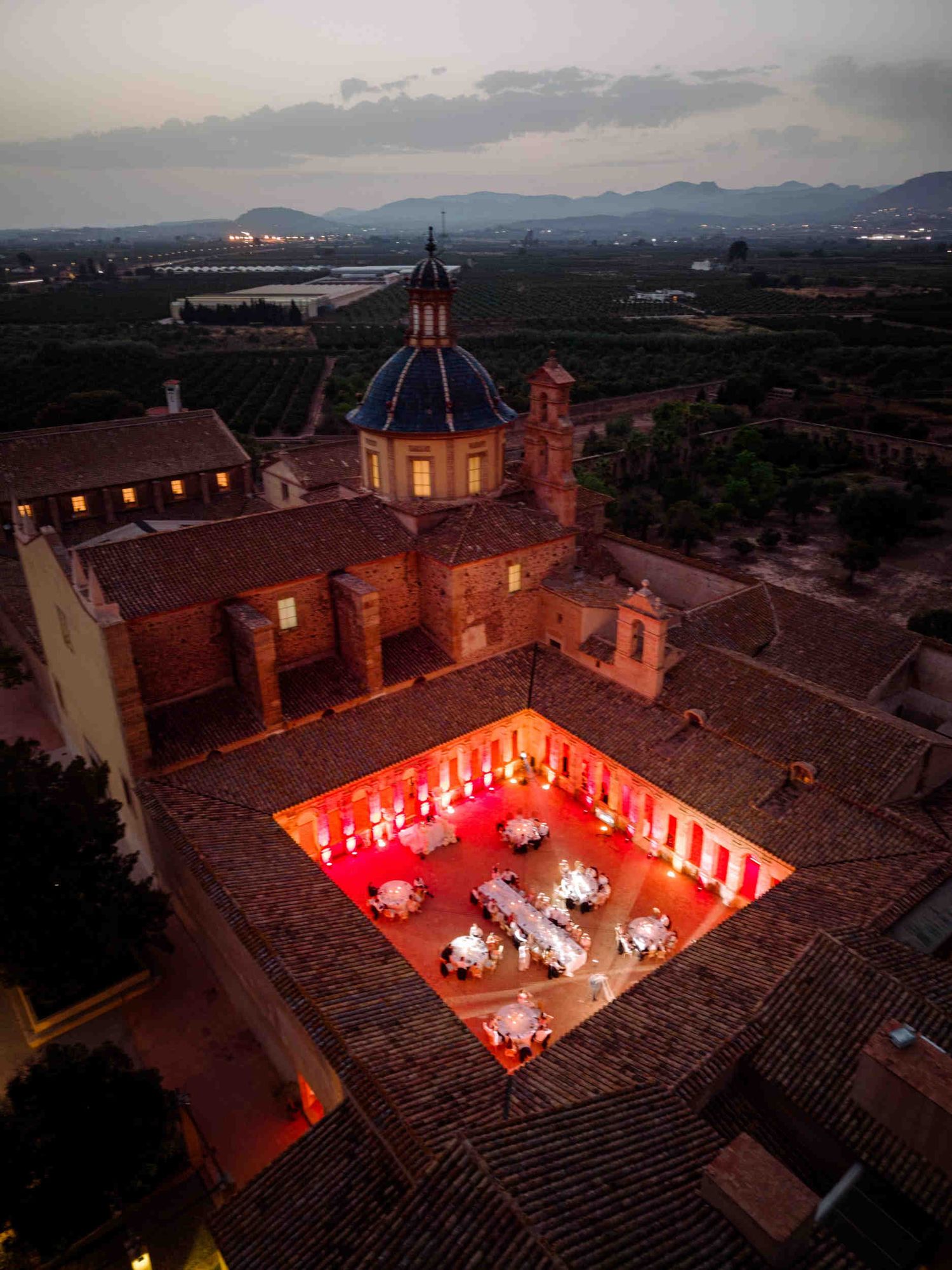 Aerial twilight view of La Cartuja de Ara Christi, showing the historic dome and a wedding reception glowing with red lights.