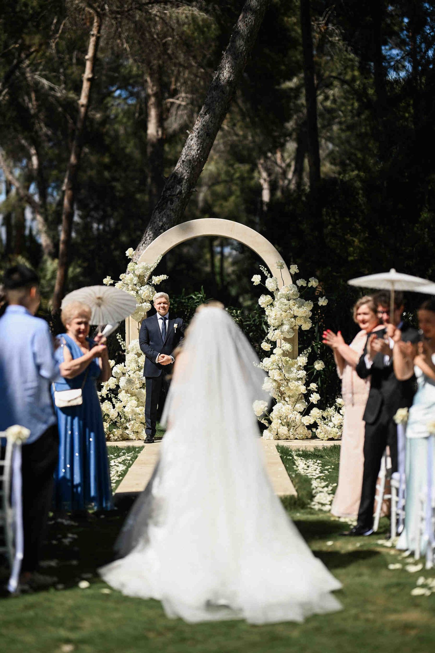 Bride walking down the aisle towards the groom standing under a floral arch at a beautiful outdoor wedding in Benidorm, Spain.