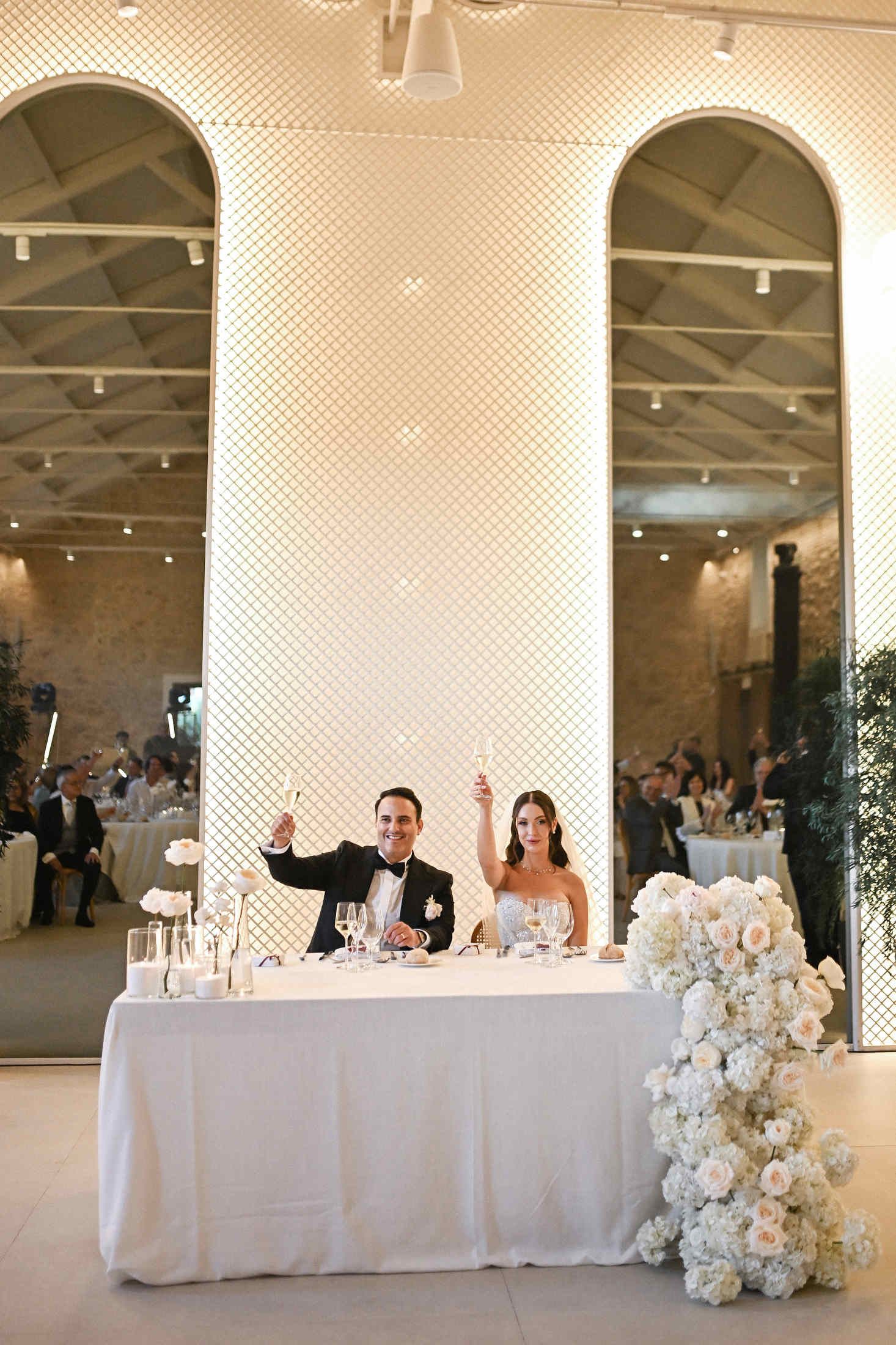 Bride and groom raising champagne glasses for a toast at their sweetheart table inside a stone hall at Finca del Canónigo.