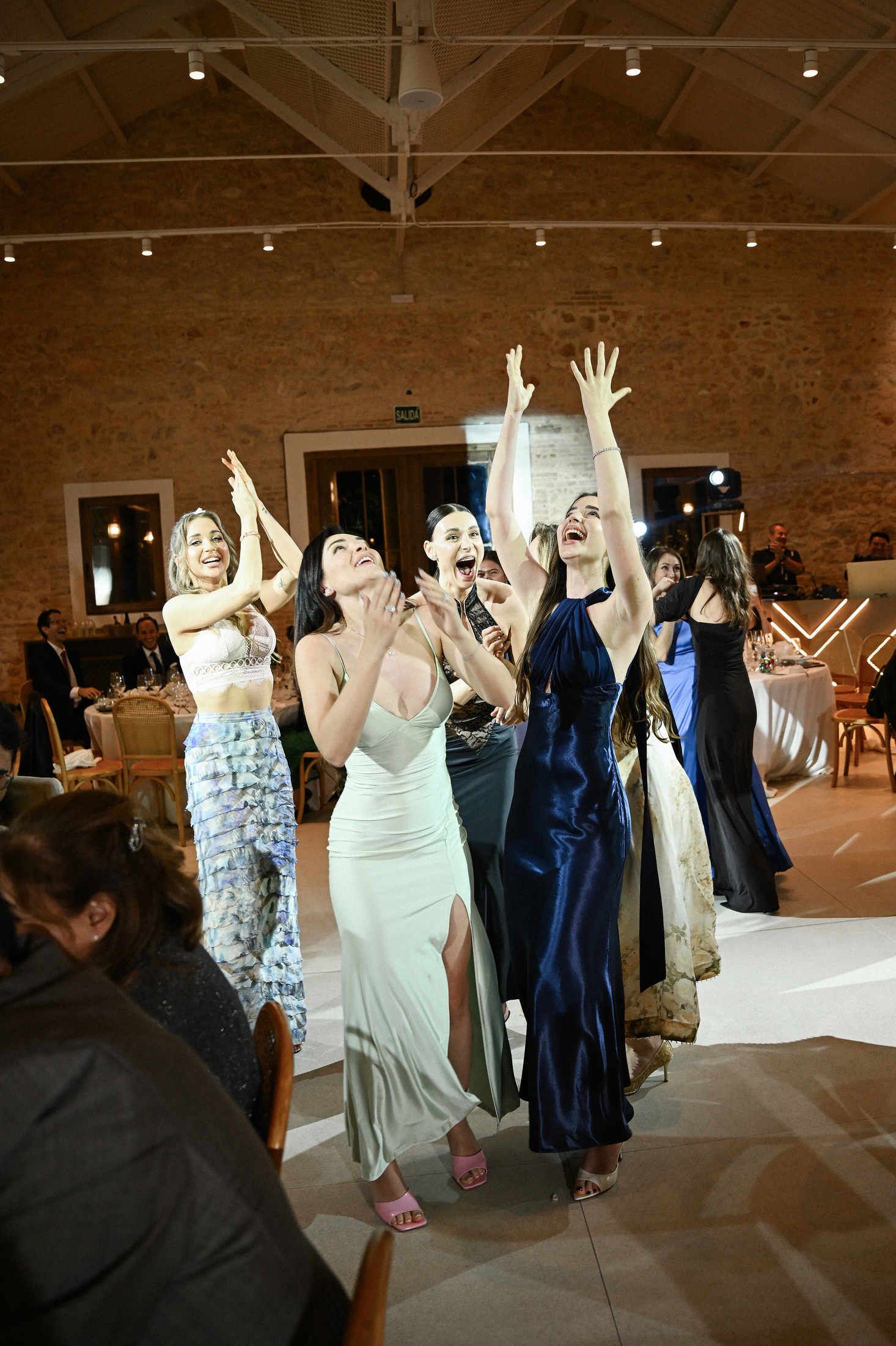 Excited female guests laughing and reaching up to catch the bridal bouquet at an elegant wedding party in finca del canonigo hall