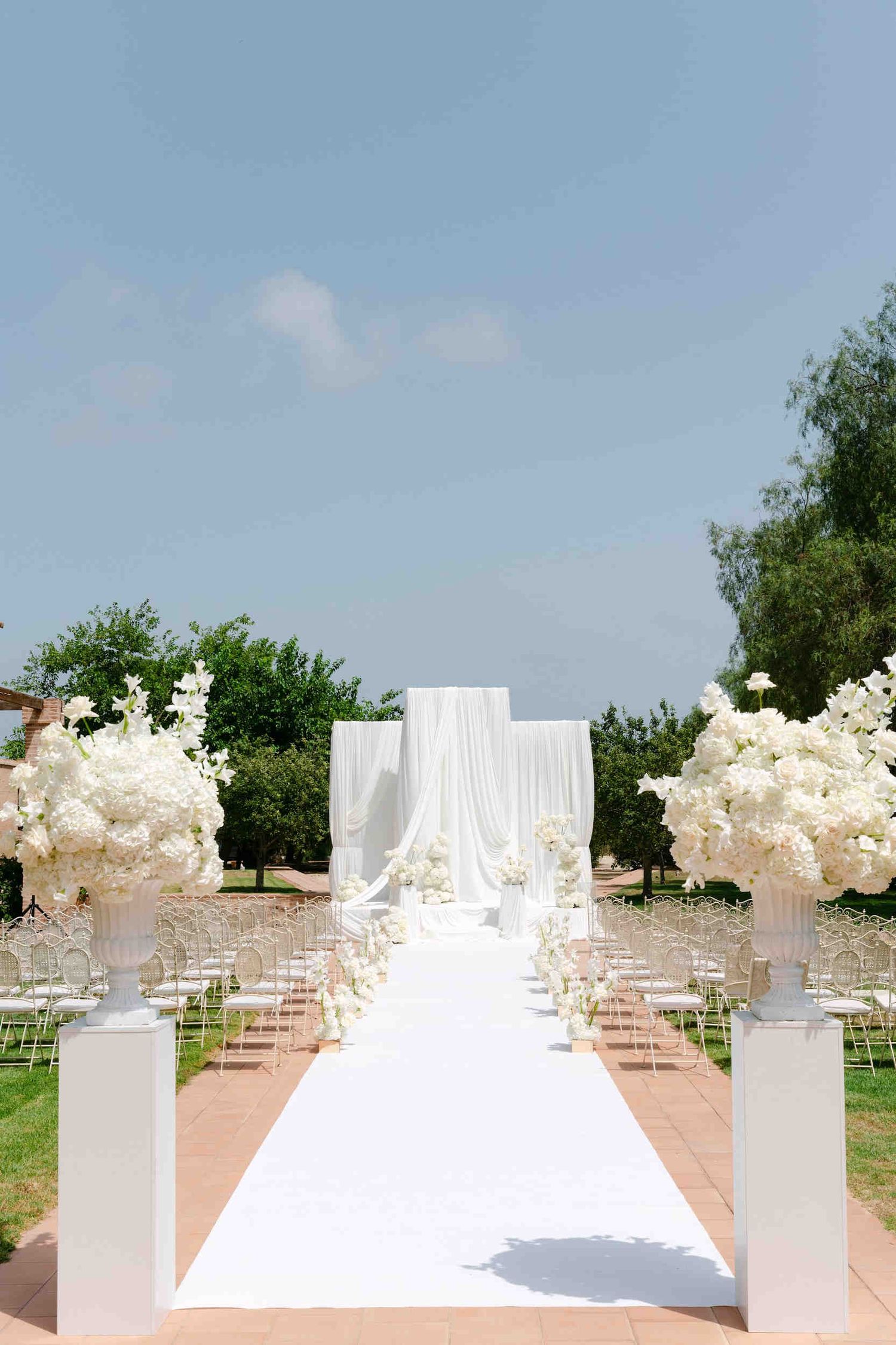 Outdoor wedding ceremony altar draped in white fabric with floral arrangements at La Cartuja de Ara Christi.