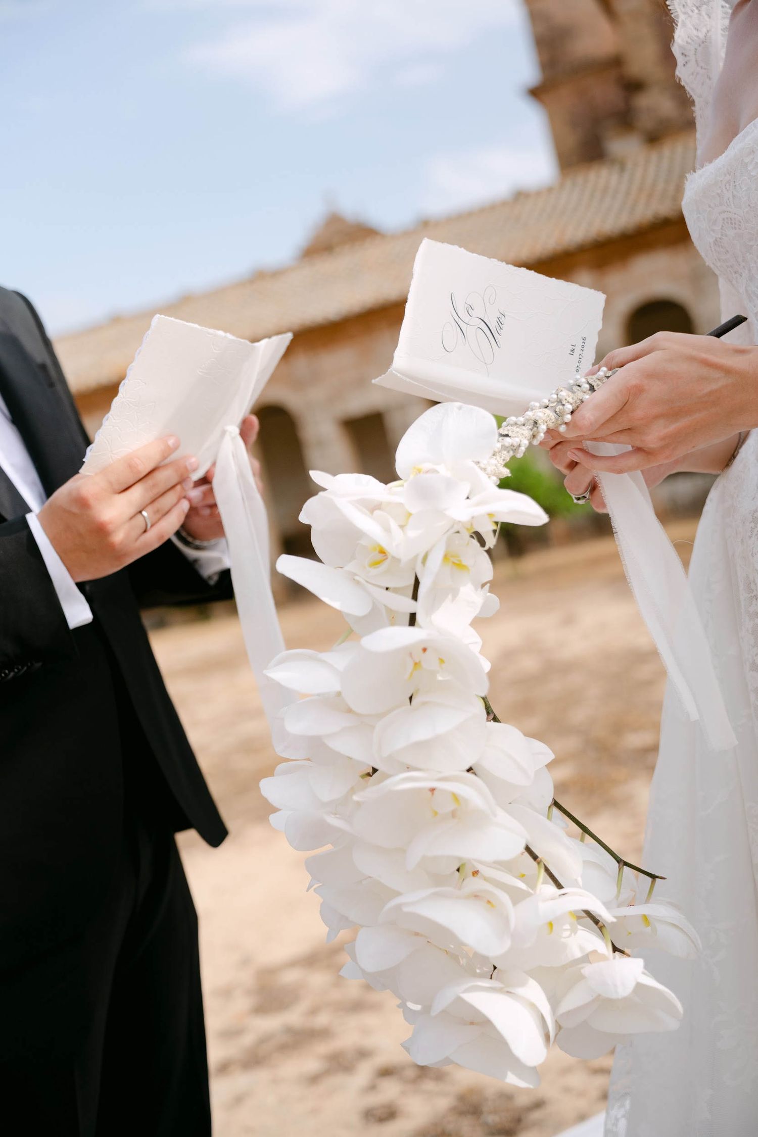 Close-up of a bride holding a white orchid bouquet and a groom with vow books during their La Cartuja de Ara Christi ceremony.