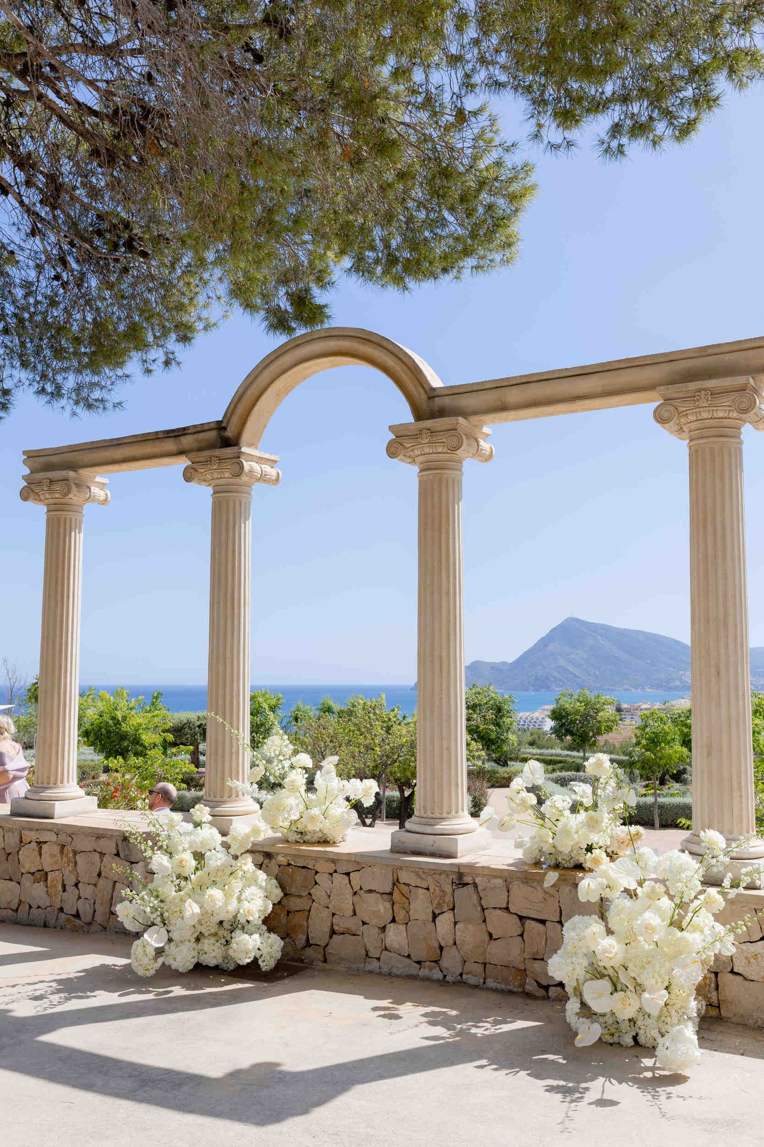 Stunning outdoor wedding ceremony terrace with stone pillars, white floral arrangements, and Mediterranean Sea views in Altea.